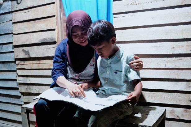 Wiwik Handayani (kiri), warga Sungai Kunyit, Mempawah, Kalimantan Barat sedang menemani anaknya belajar di rumahnya pada malam hari pasca dirinya menerima bantuan penyambungan listrik gratis melalui program Light Up The Dream PLN.